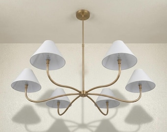 May include: A six-light chandelier featuring a central brass-toned metal rod and curved arms extending outwards. Each arm supports a white, conical fabric lampshade. The fixture is suspended from a matching circular brass-toned ceiling canopy.