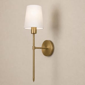 K&ouml;nnte beinhalten: Eine Wandleuchte mit einem schlanken Arm aus geb&uuml;rstetem Messing und einer runden Wandhalterung. Die Leuchte ist mit einem konischen, wei&szlig;en Stoffschirm ausgestattet, der das Licht nach unten lenkt, und besitzt ein vertikales Design mit Endst&uuml;ck.