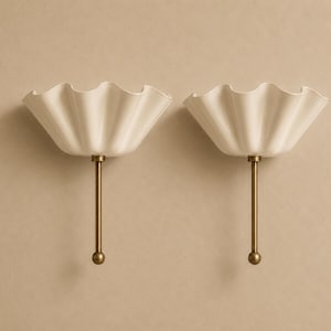 Peut inclure: Une paire d'appliques murales composées d'abat-jours en forme de bol blanc cassé aux bords ondulés, fixés sur de fines tiges métalliques verticales de couleur laiton. Chaque tige se termine par un petit embout sphérique à la base.