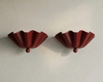 May include: Two wall sconces in a deep red USC Cardinal finish. Each fixture features a wide, scalloped, fan-like shade with a central spherical accent at the base. The design is symmetrical, showcasing a pleated, wavy edge profile.