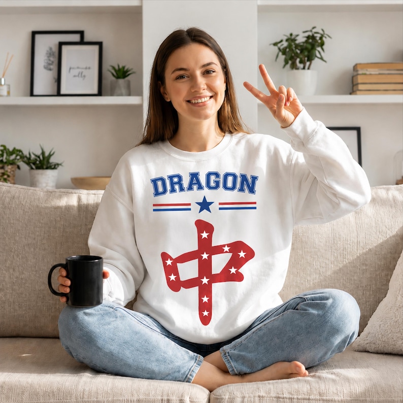 May include: A white long-sleeve sweatshirt featuring the word DRAGON in blue letters above a blue star and red and blue horizontal lines. Below this, a large red Chinese character is filled with small white stars on the front of the garment.