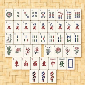 May include: A complete set of ivory-colored Mahjong tiles arranged on a woven bamboo mat. The tiles feature various suits, numbers, and Chinese characters, including dragons and directional symbols. The tiles are decorated with red, green, and blue details.