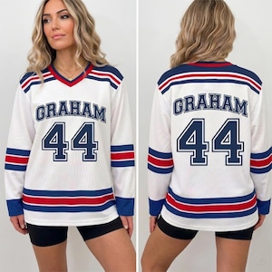 May include: A white long-sleeve jersey featuring a V-neck collar, blue and red horizontal stripes on the sleeves and hem, and the name GRAHAM with the number 44 printed in blue on both the front and back of the garment.