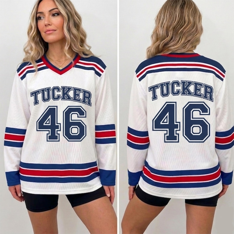 May include: A white long-sleeve jersey with a V-neck collar, featuring the name TUCKER and the number 46 in navy blue with white outlines. The sleeves and hem have horizontal stripes in navy blue and red. The fabric has a mesh texture.
