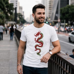 May include: White t-shirt featuring a red and green dragon design. The dragon is depicted in a vertical, stylized manner, with intricate details. The shirt is a classic crew neck style, made of a soft material.