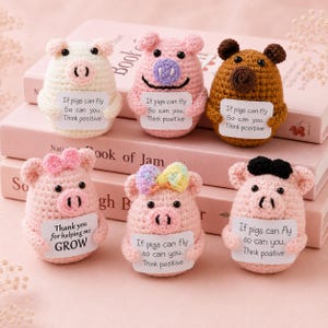 May include: Six small, round, crocheted pig figurines in various colors including cream, pink, and brown. Each pig features black bead eyes, a snout, and holds a small white card with printed text such as "If pigs can fly so can you. Think positive" or "Thank you for helping me GROW."