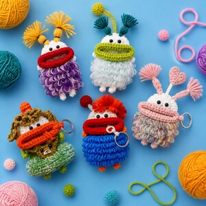 May include: Five colorful crocheted monster keychains with large eyes and wide mouths. Each creature features unique yarn textures, including loops and tufts, in shades of purple, white, green, blue, and multicolored yarn, each attached to a metal ring.