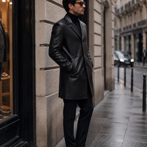 May include: A black leather coat with a notched lapel, long sleeves, and a button-front closure. The coat is worn over a black turtleneck sweater and black trousers, paired with black leather dress shoes and dark-tinted sunglasses.