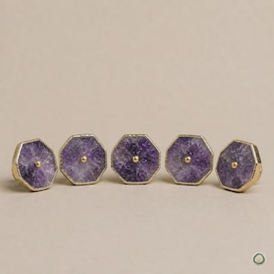 Puede incluir: Cinco pomos octogonales para armarios con rodajas de piedra amatista morada natural, bordes de metal dorado texturizado y un pequeño perno de metal dorado centrado en la parte frontal de cada pieza, dispuestos en una fila horizontal.