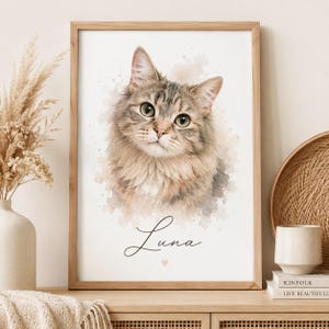 May include: A framed watercolour-style portrait of a long-haired tabby cat with green eyes. The artwork features a soft, neutral-toned background with a paint-splatter effect. Below the cat, the name Luna is written in black script with a small heart.