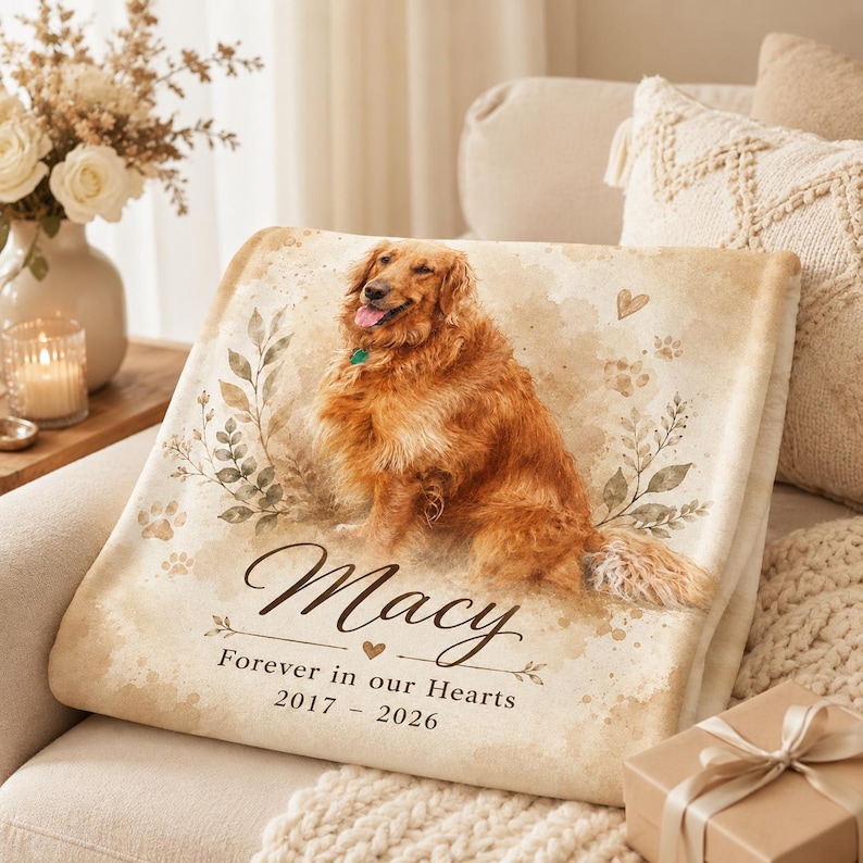 K&ouml;nnte beinhalten: Eine cremefarbene Fleecedecke mit dem Aufdruck eines Golden Retrievers, Aquarell-Blattmotiven und Pfotenabdr&uuml;cken. Der Text lautet: Macy, Forever in our Hearts, 2017 - 2026. Das Design enth&auml;lt ein kleines Herzsymbol und dekorative Verzierungen.