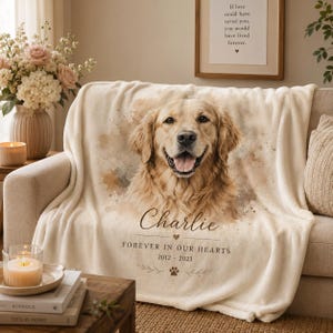 Könnte beinhalten: Eine cremefarbene Fleecedecke mit einem golden Retriever-Porträt im Aquarellstil. Der Text lautet Charlie, Forever in our hearts, 2012-2023, ergänzt durch ein kleines Herzsymbol und eine Pfotenabdruck-Grafik, die unter dem Hund zentriert sind.