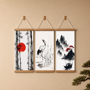 Peut inclure: Trois impressions d'art de style japonais encadrées. Les impressions représentent une forêt de bambous avec un soleil rouge, une grue dans l'eau et un paysage de montagne avec un bateau. Chaque impression est suspendue par une ficelle.
