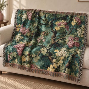 May include: A woven throw blanket featuring a detailed botanical pattern of dark green foliage, yellow leaves, and clusters of pink and white flowers. The rectangular textile has a fringed edge along all four sides and a textured finish.