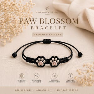 May include: A black cord bracelet featuring two small paw print motifs with light pink pads and black outlines. The bracelet has an adjustable sliding knot closure with two small black spherical beads at the ends. Text reads PAW BLOSSOM BRACELET.