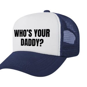 May include: A navy blue and white trucker cap featuring a white front panel with the black text WHO'S YOUR DADDY? printed in a bold sans-serif font. The cap includes a navy blue peak and a breathable navy blue mesh back with an adjustable snap closure.