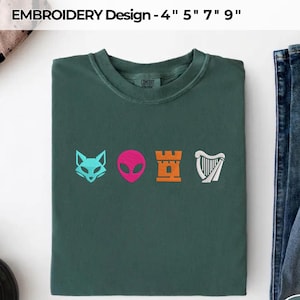 May include: A dark green crewneck t-shirt featuring four embroidered icons in a horizontal row: a light blue fox head, a bright pink alien face, an orange castle tower, and a white harp. The text EMBROIDERY Design - 4" 5" 7" 9" is visible.