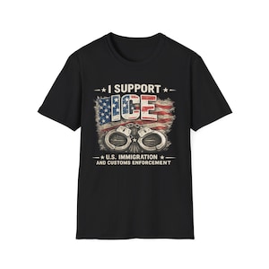 Könnte beinhalten: Ein schwarzes Kurzarm-T-Shirt mit einem Grafikdruck, der den Text I SUPPORT ICE und U.S. IMMIGRATION AND CUSTOMS ENFORCEMENT zeigt. Das Design enthält eine abgenutzte amerikanische Flagge im Hintergrund und ein Paar silberfarbene Metallhandschellen.