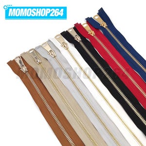 Könnte beinhalten: Eine Ansammlung von sechs Reißverschlüssen, die diagonal angeordnet sind und goldfarbene Metallzähne sowie Schieber aufweisen. Die Stoffbänder sind in Braun, Beige, Hellgrau, Weiß, Schwarz, Rot und Dunkelblau gehalten. Der Text MOMOSHOP264 ist zu sehen.
