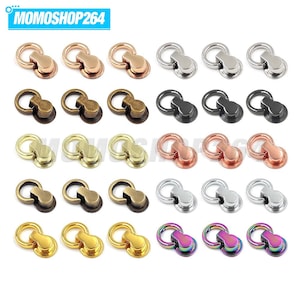 May include: A collection of thirty metal bag hardware connectors arranged in five rows of six. Each piece features a circular ring attached to a flat, rounded base. The set includes various metallic finishes: rose gold, silver, antique bronze, black, gold, copper, and iridescent rainbow.