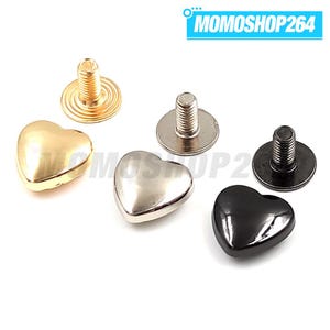 Könnte beinhalten: Drei herzförmige Metallnieten mit Schraubverschluss in Gold, Silber und Schwarz. Jede Niete hat eine glatte, abgerundete Herzoberseite und einen Gewindestift mit einer runden Basis. Der Text MOMOSHOP264 ist in der oberen rechten Ecke sichtbar.