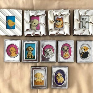 Peut inclure: Une collection de onze petits cadres photo rectangulaires de couleur argentée, contenant chacun une illustration unique dessinée à la main. Les dessins représentent divers chiens, un poussin jaune et un chat, dans des fenêtres ovales ou rectangulaires.