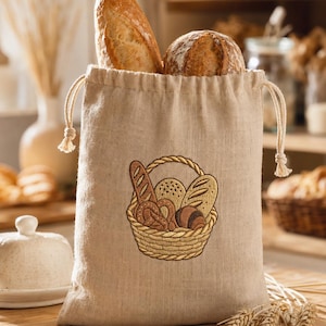 Könnte beinhalten: Ein beigefarbener Leinenbeutel mit Kordelzug, der mit einer Stickerei eines geflochtenen Korbs voller verschiedener Brotsorten wie Baguette, Brezel und runden Laiben verziert ist. Zwei knusprige Brotlaibe ragen oben aus dem Stoffbeutel heraus.