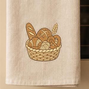 Può includere: Un canovaccio da cucina in lino beige con un ricamo raffigurante un cesto intrecciato pieno di vari tipi di pane, tra cui una baguette, una pagnotta rotonda e un pretzel, arricchito da una spiga di grano nei toni del marrone e dell'oro.