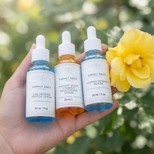 May include: Three glass dropper bottles labeled Earthly Grace. The left bottle contains blue liquid labeled Line Defense Peptide Serum 30 ml 1 fl oz. The center bottle contains orange liquid labeled Radiant Glow Vitamin C Brightening Serum 30 ml 1 fl oz. The right bottle contains blue liquid labeled Copper Renewal Serum 30 ml 1 fl oz.