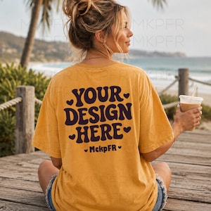 May include: A mustard yellow short-sleeve t-shirt with dark brown text on the back that reads YOUR DESIGN HERE and MckpFR, accented by small heart icons. The shirt features a crew neckline and a relaxed fit, shown from a rear perspective.