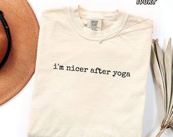 May include: An ivory short-sleeved t-shirt featuring the black text 'i'm nicer after yoga' printed on the chest. The shirt has a crew neckline and a Comfort Colors brand label on the inside collar. The color is labeled as ivory.