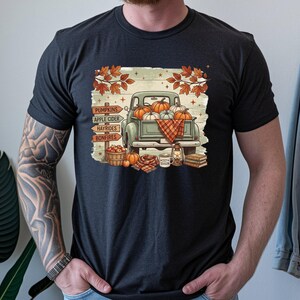 Może przedstawiać: Czarny t-shirt z grafiką przedstawiającą zabytkowy zielony pickup załadowany dyniami. Wzór zawiera drewniany drogowskaz z napisami PUMPKINS, APPLE CIDER, HAYRIDES i BONFIRES, a także kosz z jabłkami, latarnię oraz stos książek.