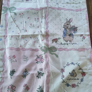 May include: A rectangular fabric panel featuring a patchwork design with pink ribbon borders and green bows. The pattern includes illustrations of rabbits, floral motifs, and the text "happy easter" and "Sylvia Serbin" in cursive script.