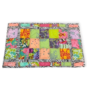 May include: A colorful patchwork quilt with a zebra-striped border. The quilt features squares of various floral patterns in shades of pink, orange, green, and purple. The quilt is a vibrant and eye-catching textile.