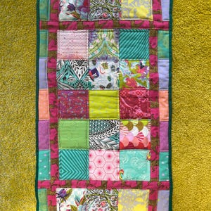 May include: A rectangular patchwork quilt featuring a variety of colorful fabric squares with diverse patterns including floral, geometric, and animal prints. The quilt is bordered by a dark pink fabric strip with a repeating leopard print pattern.