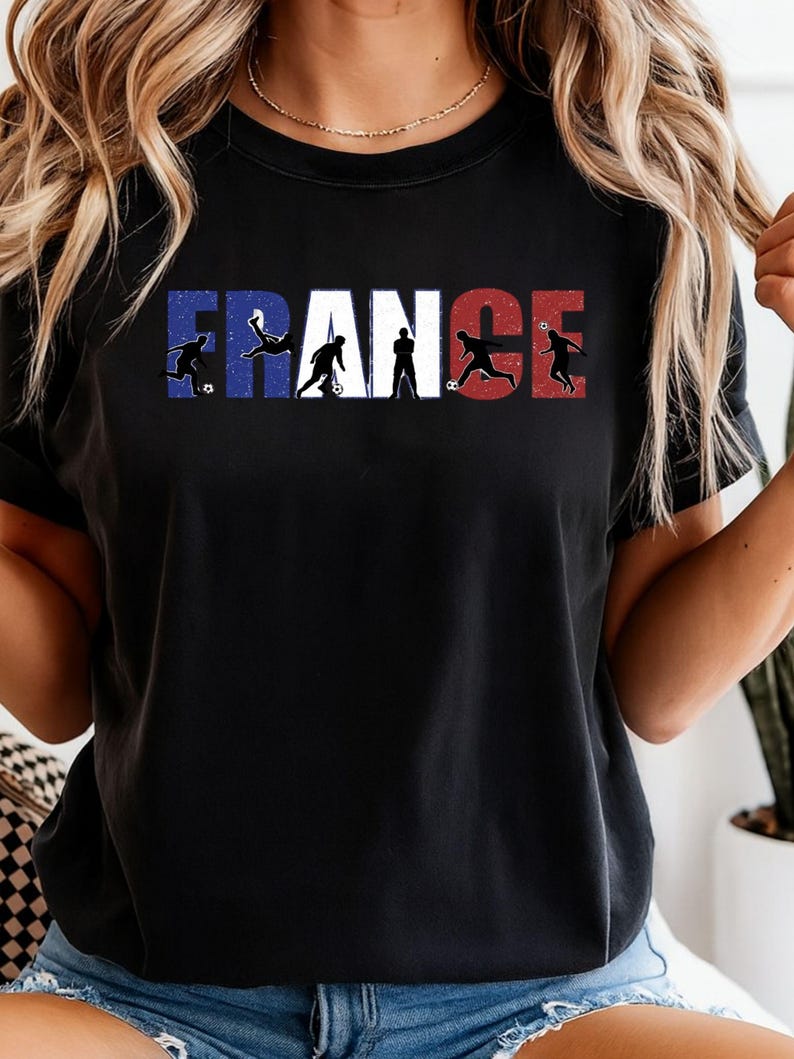 May include: Black t-shirt featuring the word "FRANCE" in the colors of the French flag. The letters are interspersed with silhouettes of soccer players in action, creating a dynamic and patriotic design. A stylish tee for soccer fans.