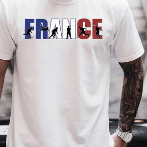 May include: White t-shirt featuring the word "FRANCE" in blue and red, with black silhouettes of soccer players incorporated into the letters. The shirt has a crew neck and short sleeves.