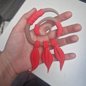 Peut inclure: Un ornement en forme de spirale composé d'une base marron lisse accentuée par des segments texturés rouge vif. Trois pendentifs rouges en forme de feuille pendent au bas de la spirale, chacun fixé par une petite pièce de connexion rouge.