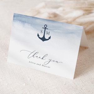 May include: A folded thank you card with a watercolor wash of blue and white. A navy blue anchor with the initials "S" and "M" is centered at the top. The words "Thank you" are written in cursive, with "Silvia and Marcus" below.