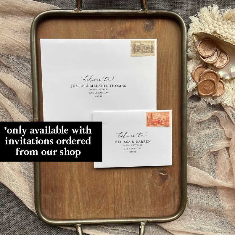 May include: Two white envelopes with black calligraphy and a handwritten address. The envelopes are on a wooden tray with a decorative shell and wax seals. The text on the envelopes reads "deliver to" followed by the name and address of the recipient. The text "*only available with invitations ordered from our shop" is written in black on a white background.