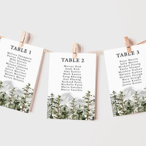 May include: Three table cards with a watercolor mountain and forest design. The cards are labeled "Table 1", "Table 2", and "Table 3" and list names for each table.