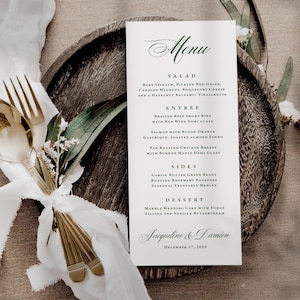 May include: A white rectangular menu card with dark green text featuring sections for salad, entree, sides, and dessert, with the names Jacqueline & Damien and the date December 17, 2029, printed at the bottom in a formal script font.