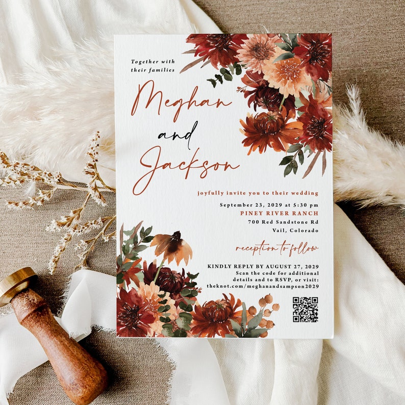May include: Wedding invitation with a floral design in shades of red, orange, and brown. The invitation features the names "Meghan and Jackson" and details for their wedding on September 23, 2029, at Piney River Ranch in Vail, Colorado. A QR code is included for additional details and RSVP.