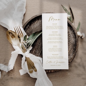 Pu&ograve; includere: Un menu di nozze con scritte dorate, con un elenco di piatti. Il menu &egrave; su una carta bianca, posta su un piatto di legno, con una forchetta e un cucchiaio dorati legati con un nastro bianco. Il menu include i nomi dei piatti.