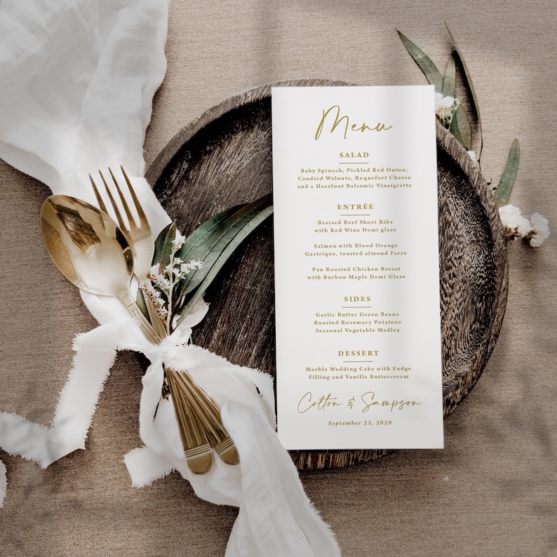 Pu&ograve; includere: Un menu di nozze con scritte dorate, con un elenco di piatti. Il menu &egrave; su una carta bianca, posta su un piatto di legno, con una forchetta e un cucchiaio dorati legati con un nastro bianco. Il menu include i nomi dei piatti.