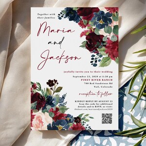 May include: A white wedding invitation card featuring watercolor floral arrangements in deep burgundy, navy blue, and soft pink. The text reads Maria and Jackson, September 23, 2029, at Piney River Ranch, 700 Red Sandstone Rd, Vail, Colorado, with a QR code.
