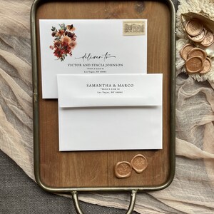 May include: A white envelope with a floral design and the text "deliver to" followed by an address. The envelope is on a wooden tray with two wax seals.