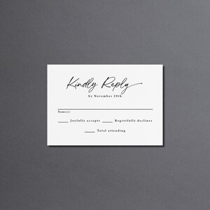 May include: A white RSVP card with black text that reads "Kindly Reply by November 29th". The card has lines for the guest's name, a check box for "Joyfully accepts", a check box for "Regretfully declines", and a line for the total number of people attending.