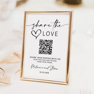 May include: A framed sign with gold trim and the words "share the LOVE" in elegant script. Below the text is a heart symbol and a QR code. The sign also includes the text "SHARE YOUR PHOTOS WITH US! SCAN THE CODE AND UPLOAD FROM YOUR PHONE."