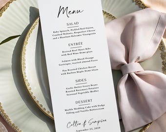 May include: A formal menu card with the word "Menu" at the top, listing salad, entree, sides, and dessert options. The menu is on a white card, placed on a decorative plate with a gold rim, and a folded pink napkin.